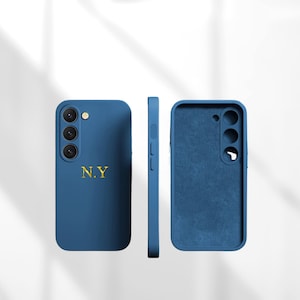 Puede incluir: Funda de teléfono azul con las letras doradas "N.Y". La funda tiene recortes para la cámara y los botones. La imagen muestra la parte delantera, lateral e interior de la funda.