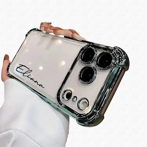 May include: Clear phone case with a metallic green frame and camera lens accents. The case has the name "Eliana" in black script. The case is designed to protect the phone's camera and body.