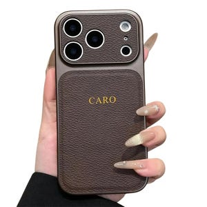 May include: Brown leather-effect phone case with a gold-coloured frame. The case has a camera cutout with multiple lenses and the word "CARO" in gold lettering. The case is designed to protect the phone and improve its appearance.