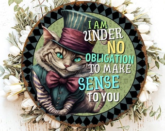 May include: Round metal sign featuring a Cheshire Cat illustration in a top hat and suit. The sign has the text "I AM UNDER NO OBLIGATION TO MAKE SENSE TO YOU" in white and teal. The cat has a mischievous grin and teal eyes. The sign is surrounded by a floral arrangement.