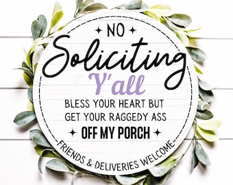 Könnte beinhalten: Ein rundes weißes Schild mit Holzmaserung, das schwarzen und violetten Text zeigt: NO SOLICITING Y'ALL BLESS YOUR HEART BUT GET YOUR RAGGEDY ASS OFF MY PORCH FRIENDS & DELIVERIES WELCOME. Das Schild ist von grünen Blättern umgeben.