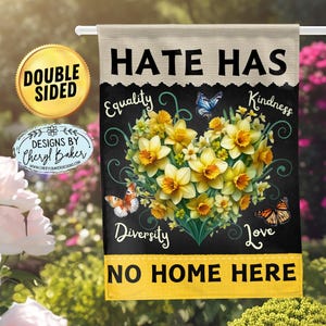 May include: Double-sided garden flag with a black background and yellow flowers in the shape of a heart. The text "Hate Has No Home Here" is written in yellow letters on a black background. The words "Equality", "Kindness", "Diversity", and "Love" are written in white letters on a black background.