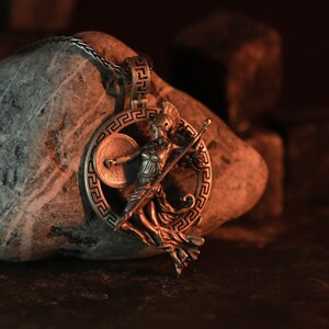 May include: Silver pendant necklace featuring a detailed depiction of a Greek goddess holding a spear and shield, set against a background of a stone.