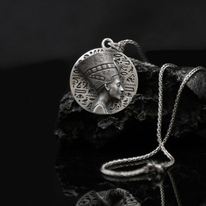 May include: Silver pendant necklace featuring a detailed profile of an Egyptian queen wearing a headdress with hieroglyphics. The pendant is round and hangs from a silver chain.