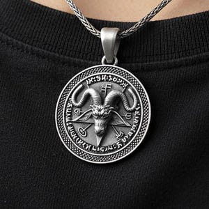 May include: Silver-toned pendant necklace featuring a detailed, circular design. The pendant showcases a goat's head within a pentagram, surrounded by intricate symbols and text. The necklace is worn against a black background.