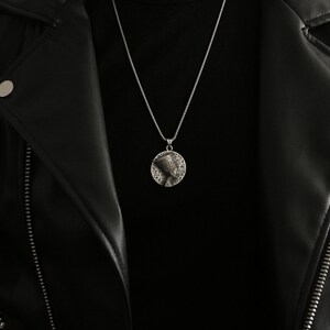 May include: A silver chain necklace with a round pendant featuring a detailed profile of an Egyptian queen. The pendant is surrounded by hieroglyphs.