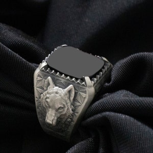 Puede incluir: Un anillo de plata con una piedra negra y un dise&ntilde;o de cabeza de lobo.