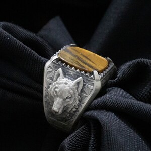 Puede incluir: Un anillo de plata con un dise&ntilde;o de cabeza de lobo y una piedra de ojo de tigre.