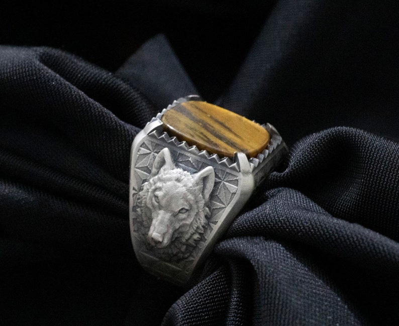Puede incluir: Un anillo de plata con un dise&ntilde;o de cabeza de lobo y una piedra de ojo de tigre.