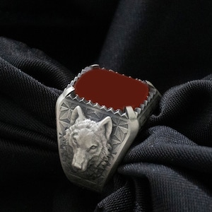 Puede incluir: Un anillo de plata con una piedra roja y un dise&ntilde;o de cabeza de lobo.