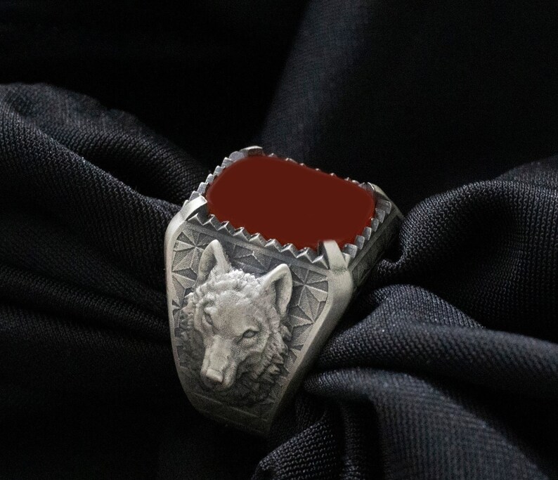 Puede incluir: Un anillo de plata con una piedra roja y un dise&ntilde;o de cabeza de lobo.