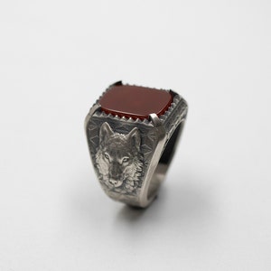 Puede incluir: Un anillo de plata con una piedra preciosa roja y un dise&ntilde;o de cabeza de lobo.