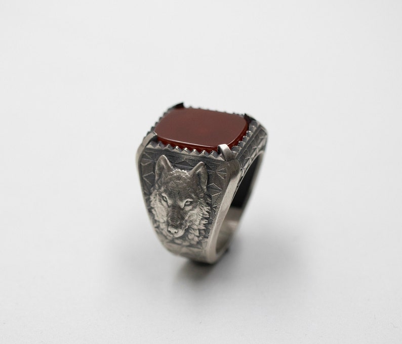 Puede incluir: Un anillo de plata con una piedra preciosa roja y un dise&ntilde;o de cabeza de lobo.