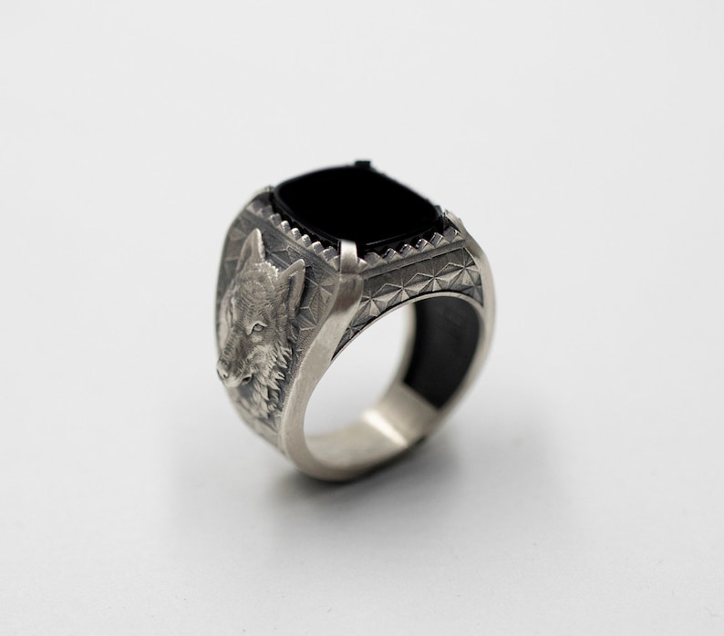 Puede incluir: Un anillo de plata con una piedra preciosa negra y un dise&ntilde;o de cabeza de lobo en el lateral.