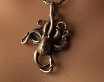 May include: A silver-toned octopus pendant with detailed tentacles and a textured body hangs from a matching chain. The pendant is centered, showcasing the intricate design of the sea creature. The necklace is a piece of jewelry.