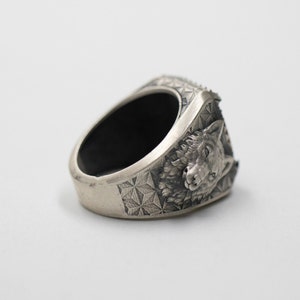Puede incluir: Un anillo de plata con un dise&ntilde;o de cabeza de lobo. El anillo est&aacute; detallado con un patr&oacute;n geom&eacute;trico y tiene una banda negra.