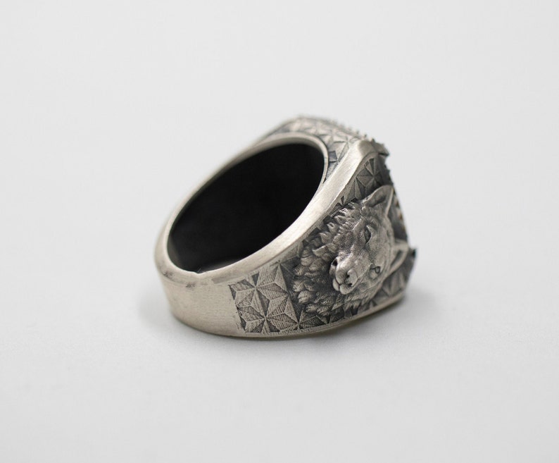 Puede incluir: Un anillo de plata con un dise&ntilde;o de cabeza de lobo. El anillo est&aacute; detallado con un patr&oacute;n geom&eacute;trico y tiene una banda negra.