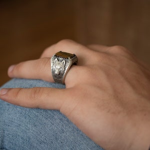 Puede incluir: Un anillo de plata con un dise&ntilde;o de cabeza de lobo y una piedra de ojo de tigre marr&oacute;n.