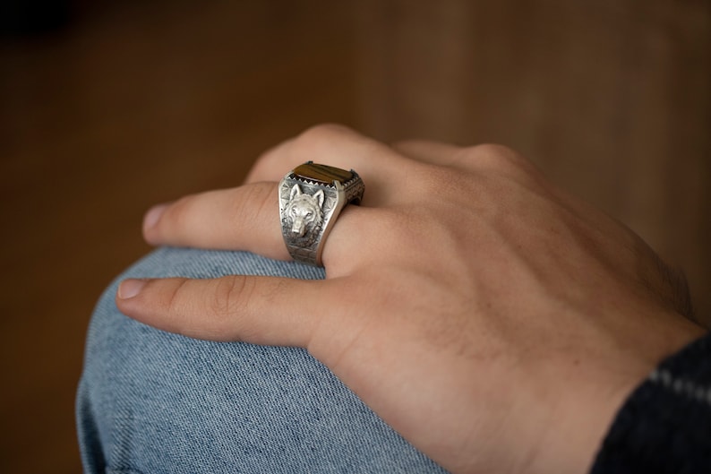 Puede incluir: Un anillo de plata con un dise&ntilde;o de cabeza de lobo y una piedra de ojo de tigre marr&oacute;n.