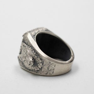 Puede incluir: Un anillo de plata con un dise&ntilde;o detallado de cabeza de lobo y un patr&oacute;n geom&eacute;trico en la banda.
