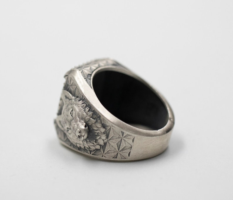 Puede incluir: Un anillo de plata con un dise&ntilde;o detallado de cabeza de lobo y un patr&oacute;n geom&eacute;trico en la banda.