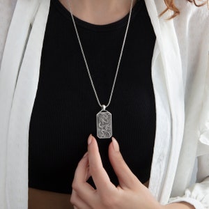 May include: A silver chain necklace with a rectangular pendant featuring a detailed dragon design.