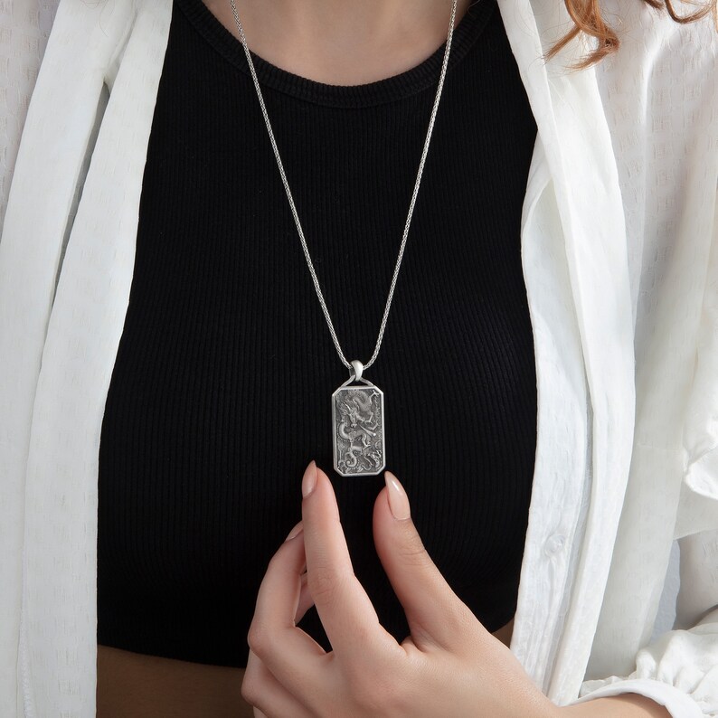 May include: A silver chain necklace with a rectangular pendant featuring a detailed dragon design.