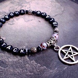 May include: Black beaded bracelet with a pentagram charm. The beads spell out "BLACK" and "ATTACK" in white lettering.