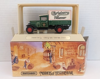 May include: A green 1932 Ford Model AA truck with a white box on the back that says "Carlsberg Pilsner" in red and black lettering. The truck is on a white base with a brown cardboard box underneath. The box has a picture of a bar with the words "Biere, Bier-Beer, Cerveza, Birra" on the side. The box also has the words "Matchbox Models of Yesteryear" on the bottom.