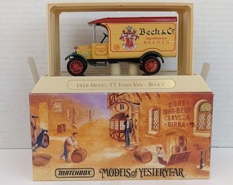 May include: A yellow and red Matchbox Models of Yesteryear die-cast toy truck, a 1926 Model TT Ford Van, with a Beck's Brewery logo. The truck is in a clear plastic display case on a box with a painted scene of a German bar.