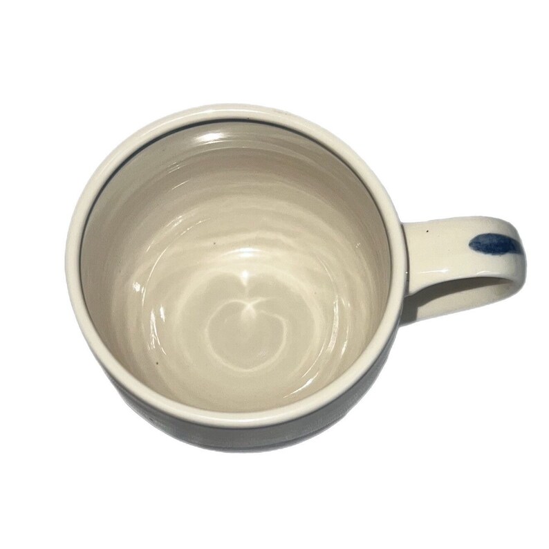 May include: A white ceramic mug with a blue rim and a blue stripe on the handle. The mug has a swirl pattern inside.