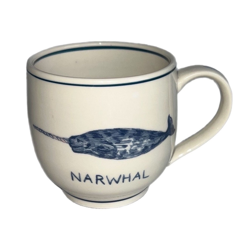 May include: A white ceramic mug with a blue narwhal illustration and the word "NARWHAL" printed on the front.