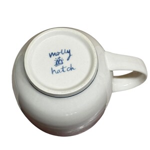 May include: White ceramic mug with a blue rim and a blue handwritten inscription that reads "molly hatch" on the bottom.