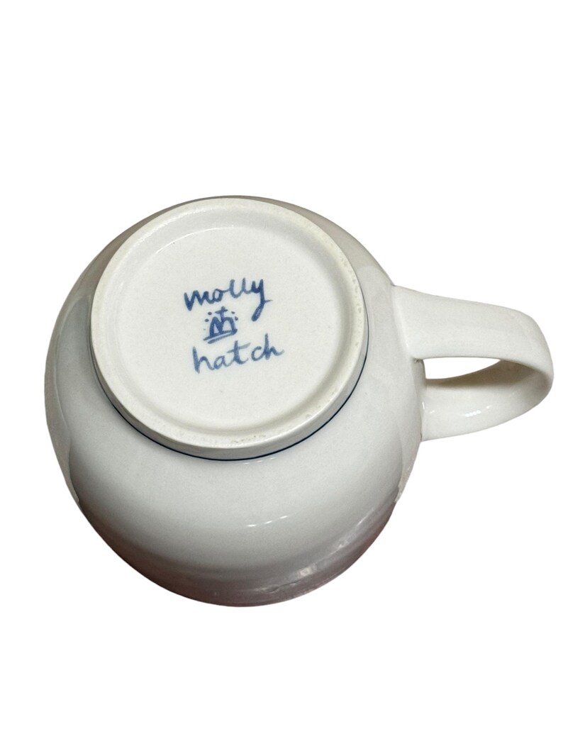 May include: White ceramic mug with a blue rim and a blue handwritten inscription that reads "molly hatch" on the bottom.