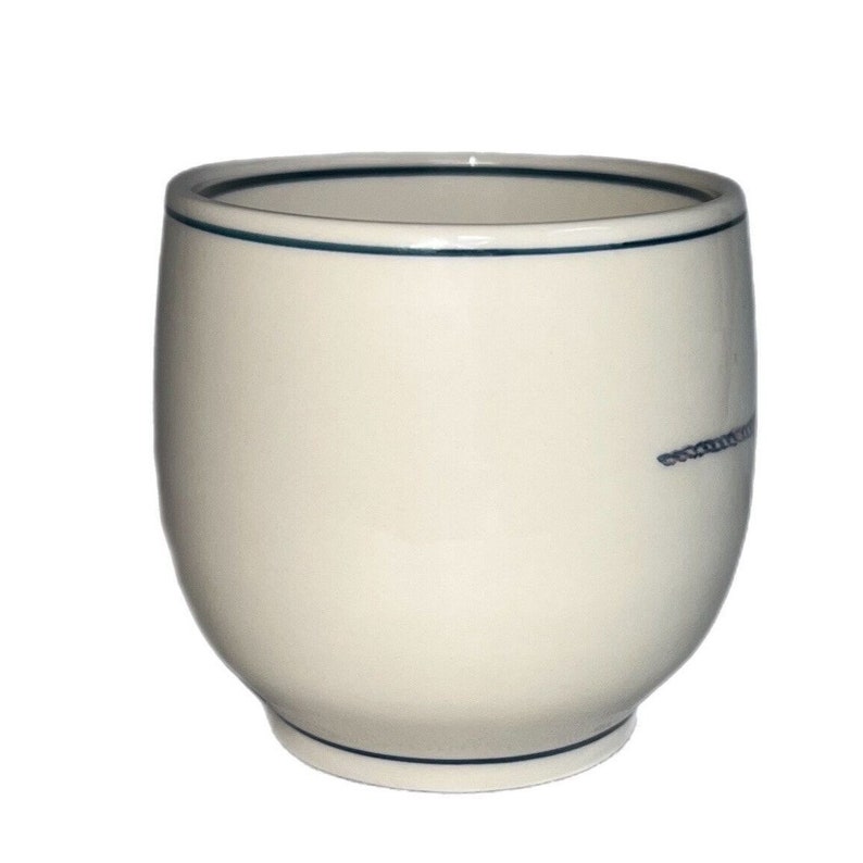 May include: A white ceramic mug with a blue rim and a thin blue line design. The mug is round and has a slightly flared lip.
