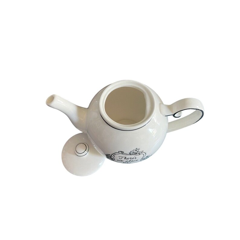 May include: White ceramic teapot with a curved handle and spout. The lid is off, revealing the interior. The teapot has a black decorative border and the text "There's no place" in a decorative frame.