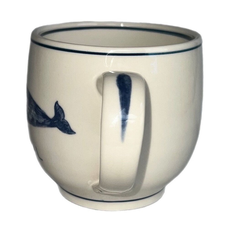 May include: A white ceramic mug with a blue whale design. The mug has a rounded shape and a handle.