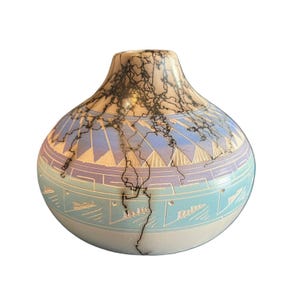 Puede incluir: Un pequeño jarrón redondo de cerámica blanca con un diseño geométrico azul y morado y un esmalte craquelado negro.