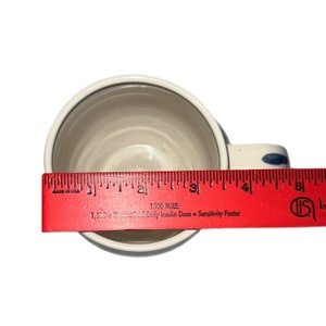 May include: A white ceramic mug with a blue and white design. The mug is 4 inches wide and has a handle.