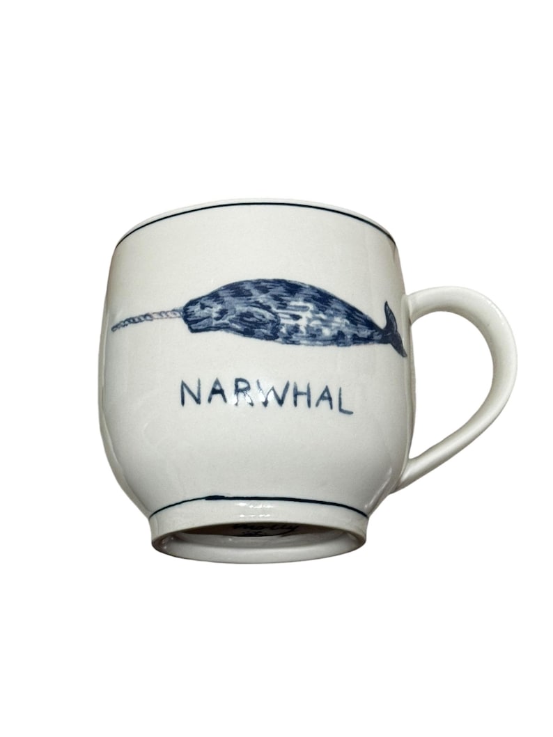 May include: White ceramic mug with a blue and black narwhal illustration and the word "NARWHAL" printed on the front.