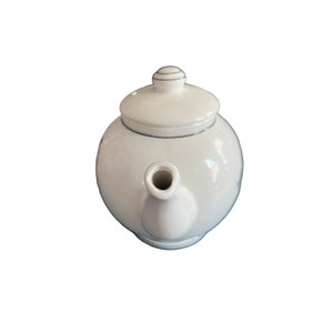 May include: A white ceramic teapot with a rounded body and a matching lid. The teapot has a spout and a handle, and is designed for brewing tea. The lid has a small knob for easy removal. The teapot is a classic design.