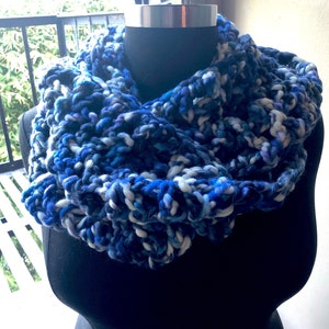 May include: A blue, white, and purple chunky knit infinity scarf. The scarf is made with a thick yarn and has a soft, cozy texture.