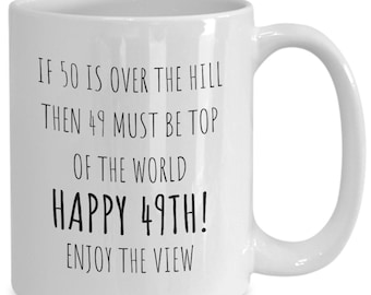 May include: White ceramic coffee mug with black text that reads "IF 50 IS OVER THE HILL THEN 49 MUST BE TOP OF THE WORLD HAPPY 49TH! ENJOY THE VIEW"
