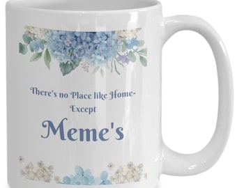 May include: White ceramic mug with a blue and white floral design. The mug has the text "There's no Place like Home - Except Meme's" printed on it.