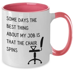 May include: White coffee mug with a pink rim and handle. The mug has black text that reads "Some days the best thing about my job is that the chair spins". A black silhouette of an office chair is below the text.
