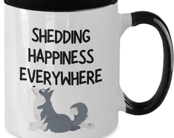 May include: White ceramic coffee mug with a black interior and handle. The mug has a black graphic that says "Shedding Happiness Everywhere" with a cartoon husky dog illustration.