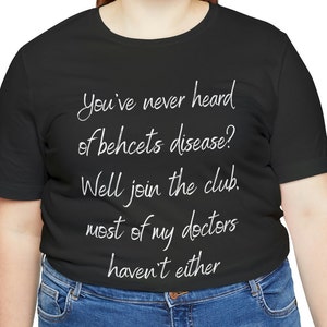May include: Black t-shirt with white script. The text reads: "You've never heard of behcets disease? Well join the club. most of my doctors haven't either."