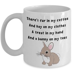 May include: White ceramic mug with a handle, featuring the text "There's fur in my coffee, And hay on my clothes, A treat in my hand, And a bunny on my toes." A cartoon bunny illustration is on the right side of the mug.