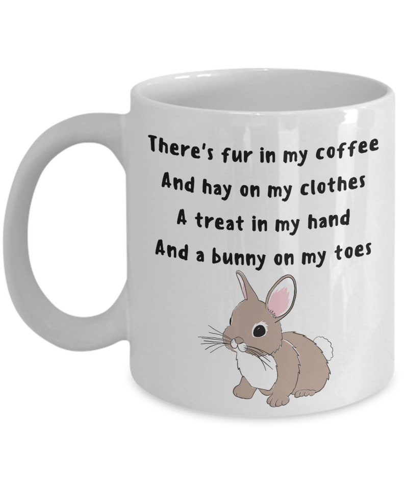 May include: White ceramic mug with a handle, featuring the text "There's fur in my coffee, And hay on my clothes, A treat in my hand, And a bunny on my toes." A cartoon bunny illustration is on the right side of the mug.