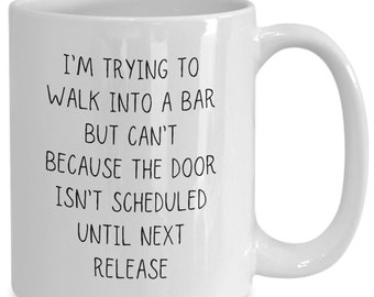 Peut inclure: Une tasse à café en céramique blanche avec du texte noir qui dit "J'essaie d'entrer dans un bar mais je ne peux pas parce que la porte n'est pas programmée avant la prochaine sortie."
